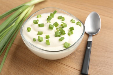 Photo of Delicious yogurt in bowl, green onions and spoon on wooden table, closeup