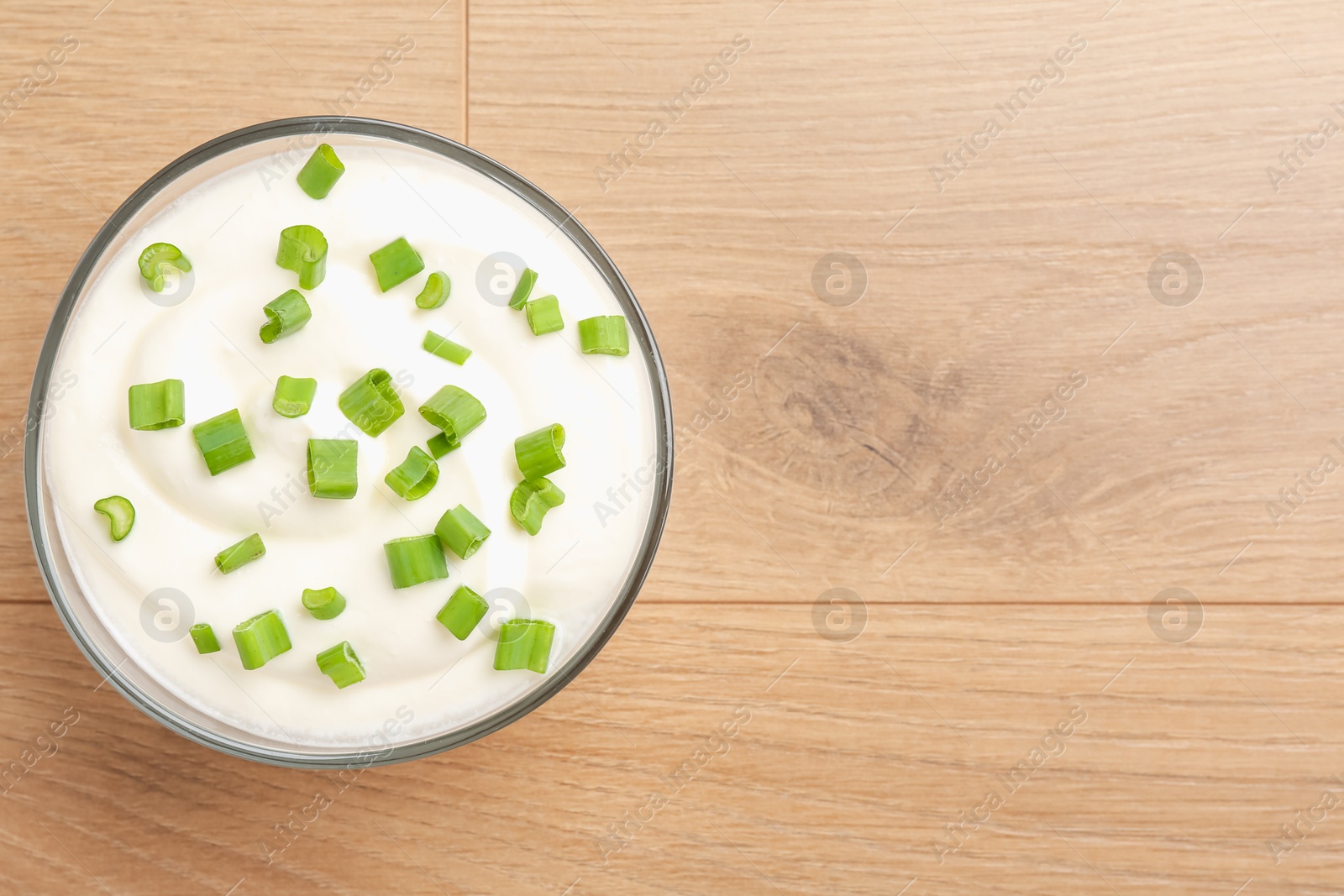 Delicious yogurt with green onions in bowl on wooden table, top view. Space for text Photo of Delicious yogurt with green onions in bowl on wooden table, top view. Space for text