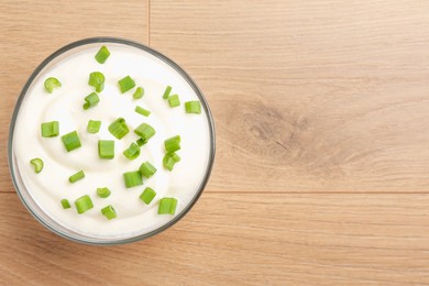 Photo of Delicious yogurt with green onions in bowl on wooden table, top view. Space for text