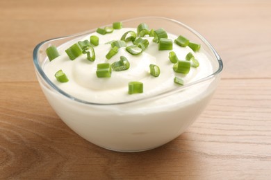 Photo of Delicious yogurt with green onions in bowl on wooden table, closeup