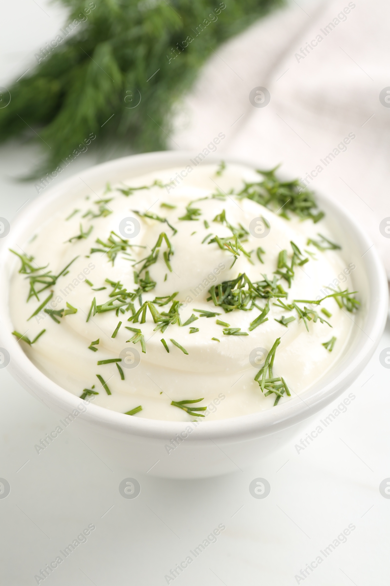 Delicious yogurt in bowl and dill on white table, closeup Photo of Delicious yogurt in bowl and dill on white table, closeup