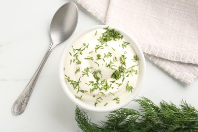 Photo of Delicious yogurt in bowl, dill and spoon on white marble table, flat lay