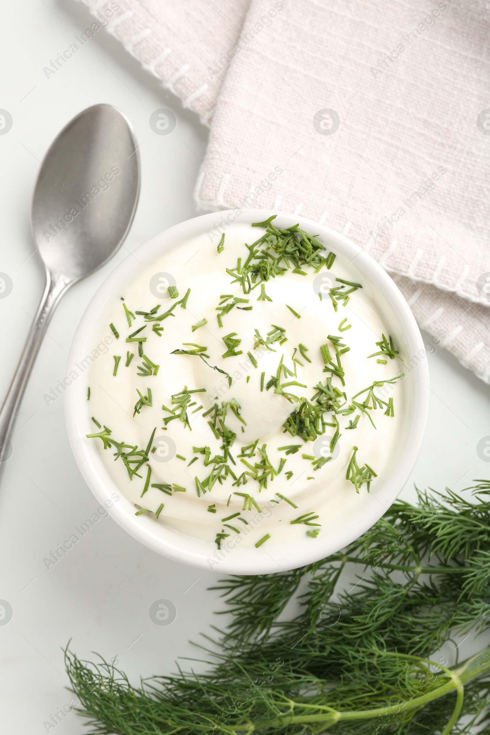 Photo of Delicious yogurt in bowl, dill and spoon on white table, flat lay