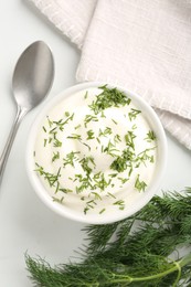 Photo of Delicious yogurt in bowl, dill and spoon on white table, flat lay