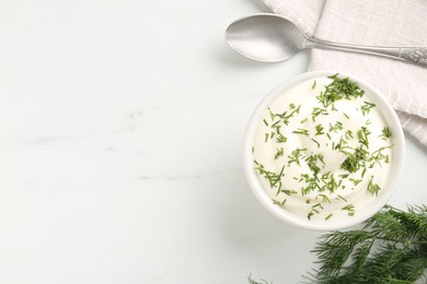 Photo of Delicious yogurt in bowl, dill and spoon on white marble table, flat lay. Space for text