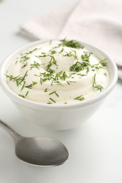 Photo of Delicious yogurt in bowl, dill and spoon on white table, closeup