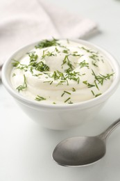 Photo of Delicious yogurt in bowl, dill and spoon on white table, closeup