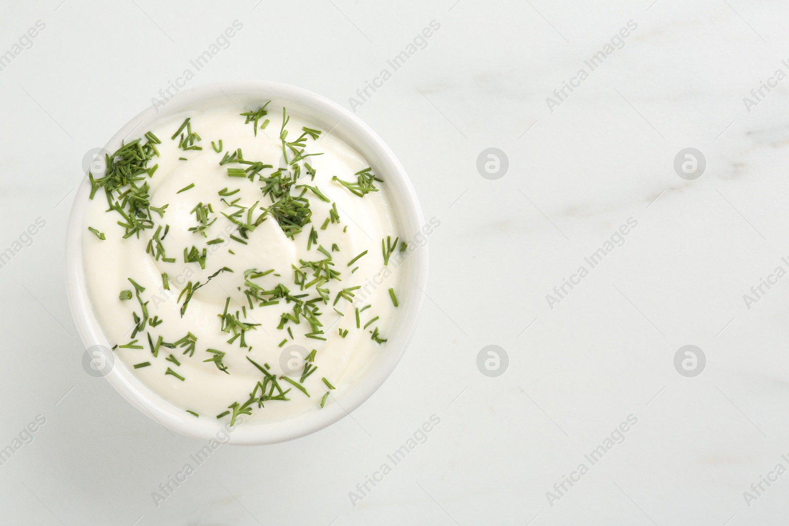 Delicious yogurt in bowl and dill on white marble table, top view. Space for text Photo of Delicious yogurt in bowl and dill on white marble table, top view. Space for text