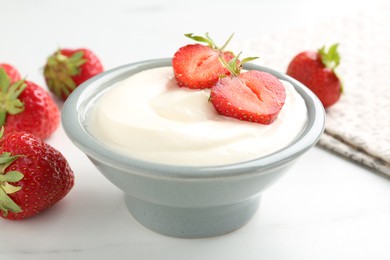 Photo of Delicious yogurt in bowl and strawberries on white marble table, closeup