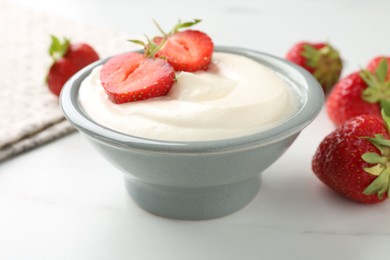 Photo of Delicious yogurt in bowl and strawberries on white marble table, closeup