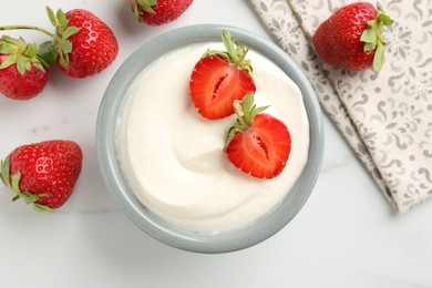 Photo of Delicious yogurt in bowl and strawberries on white marble table, flat lay
