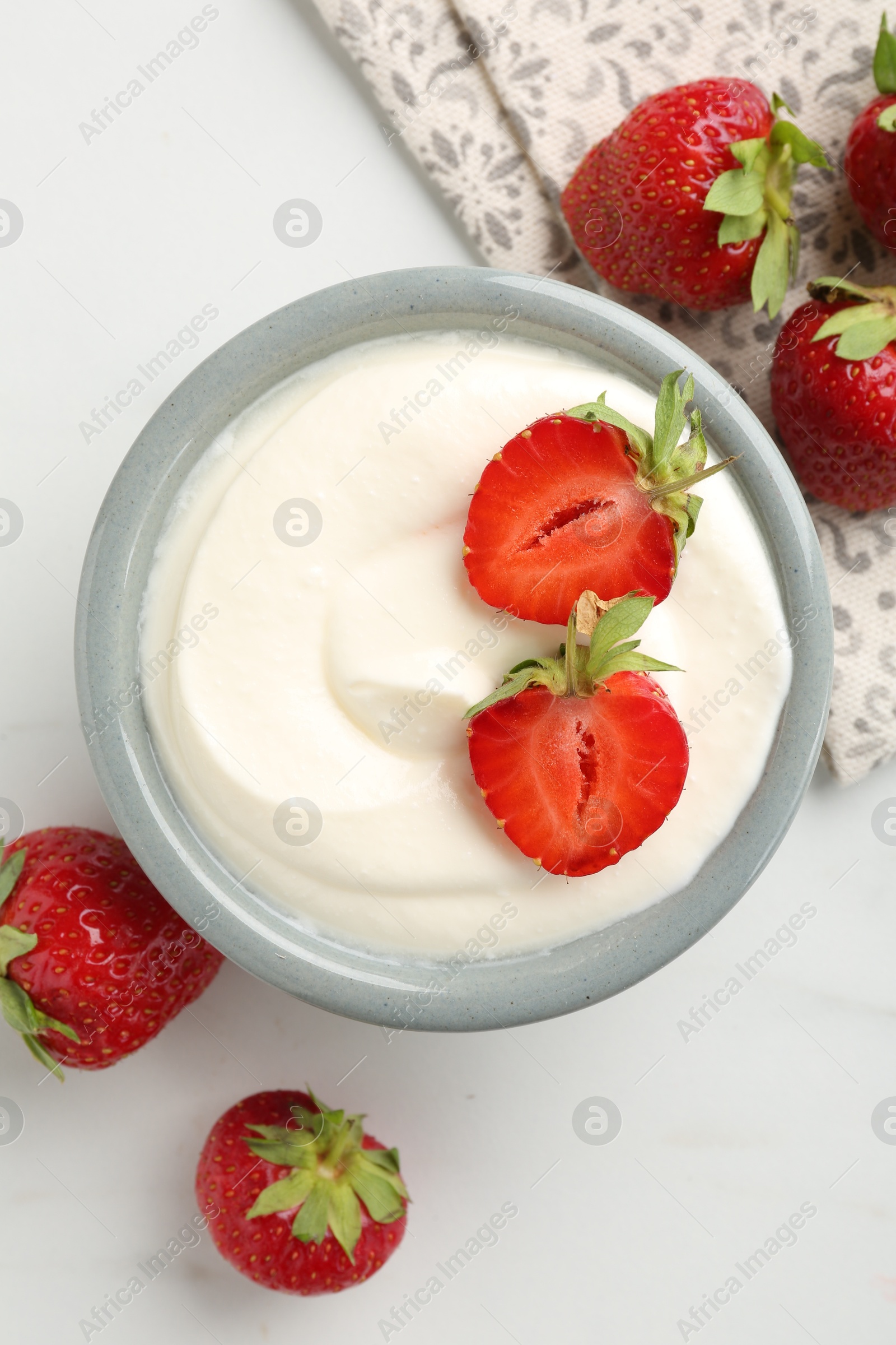Delicious yogurt in bowl and strawberries on white marble table, flat lay Photo of Delicious yogurt in bowl and strawberries on white marble table, flat lay