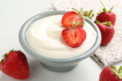 Photo of Delicious yogurt in bowl and strawberries on white table, closeup
