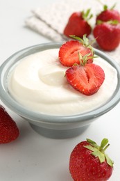 Photo of Delicious yogurt in bowl and strawberries on white table, closeup