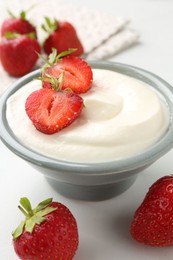 Photo of Delicious yogurt in bowl and strawberries on white table, closeup