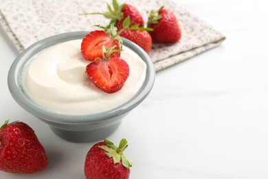 Photo of Delicious yogurt in bowl and strawberries on white marble table, closeup. Space for text
