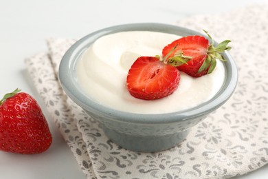 Photo of Delicious yogurt in bowl and strawberries on white table, closeup