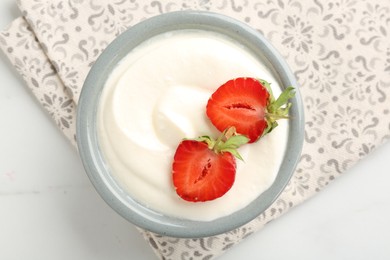 Photo of Delicious yogurt in bowl and strawberries on white marble table, top view