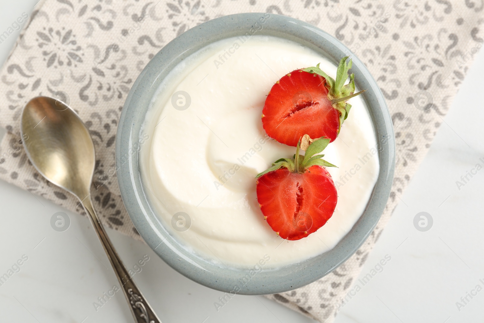 Photo of Delicious yogurt in bowl, strawberries and spoon on white table, flat lay