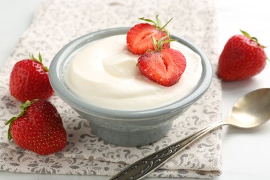 Photo of Delicious yogurt in bowl, strawberries and spoon on table, closeup