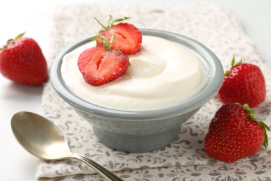Photo of Delicious yogurt in bowl, strawberries and spoon on table, closeup