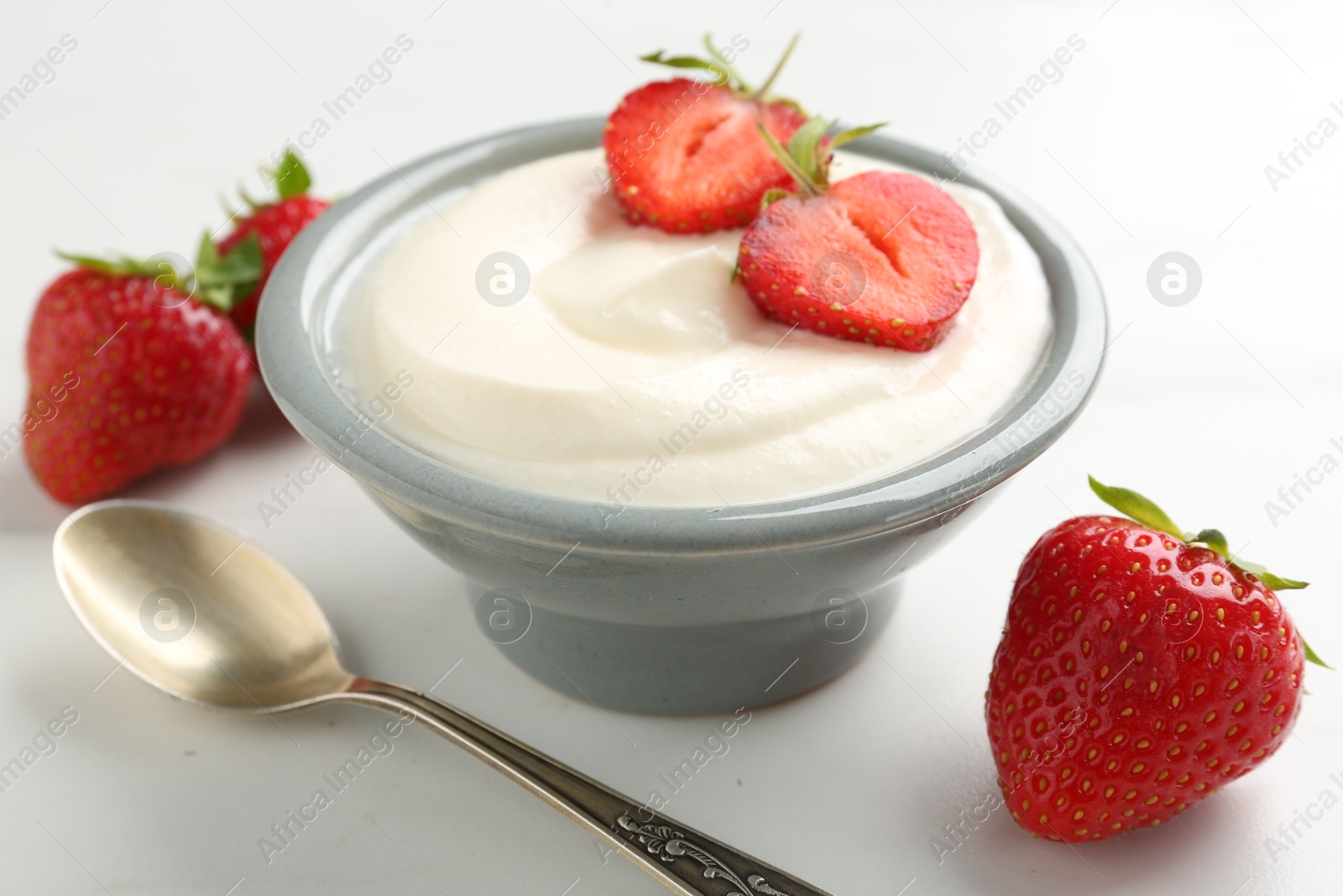 Delicious yogurt in bowl, strawberries and spoon on white table, closeup Photo of Delicious yogurt in bowl, strawberries and spoon on white table, closeup