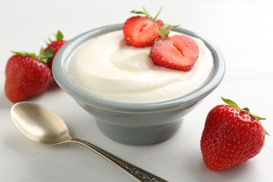 Photo of Delicious yogurt in bowl, strawberries and spoon on white table, closeup