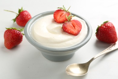 Photo of Delicious yogurt in bowl, strawberries and spoon on white table, closeup