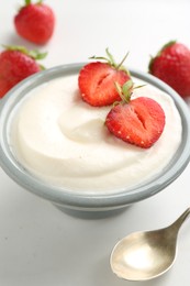 Photo of Delicious yogurt in bowl, strawberries and spoon on white table, closeup