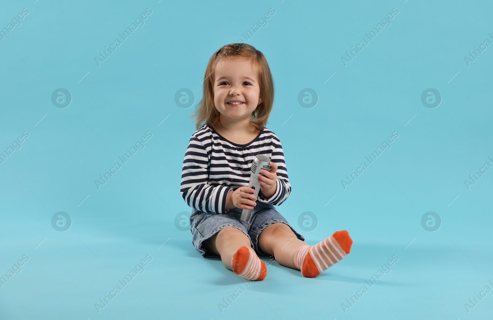 Cute little girl with microphone on light blue background Photo of Cute little girl with microphone on light blue background
