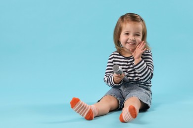 Photo of Cute little girl with microphone on light blue background, space for text