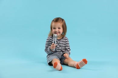 Photo of Cute little girl with microphone on light blue background