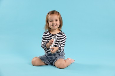 Photo of Cute little girl with microphone on light blue background