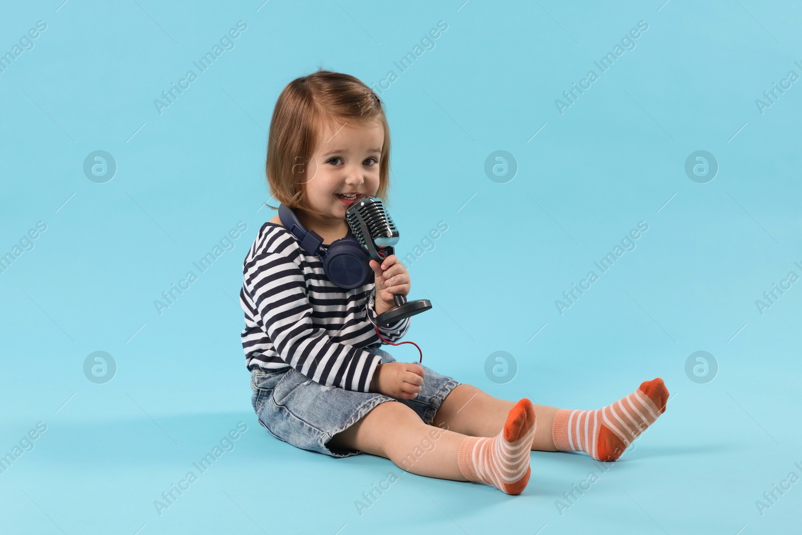 Cute little girl with headphones and microphone on light blue background Photo of Cute little girl with headphones and microphone on light blue background