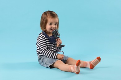 Photo of Cute little girl with headphones and microphone on light blue background