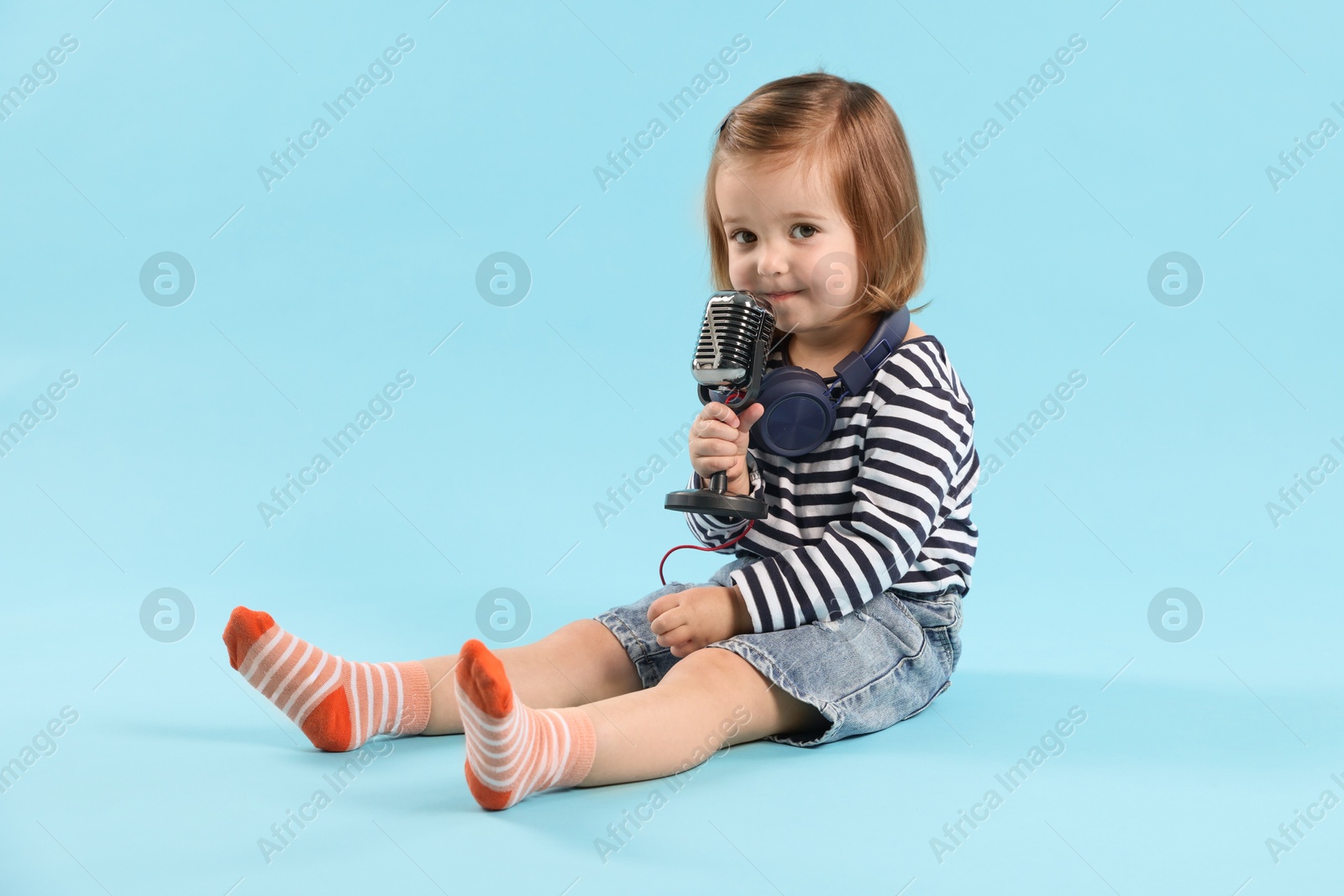 Cute little girl with headphones and microphone on light blue background Photo of Cute little girl with headphones and microphone on light blue background