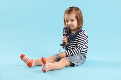 Photo of Cute little girl with headphones and microphone on light blue background