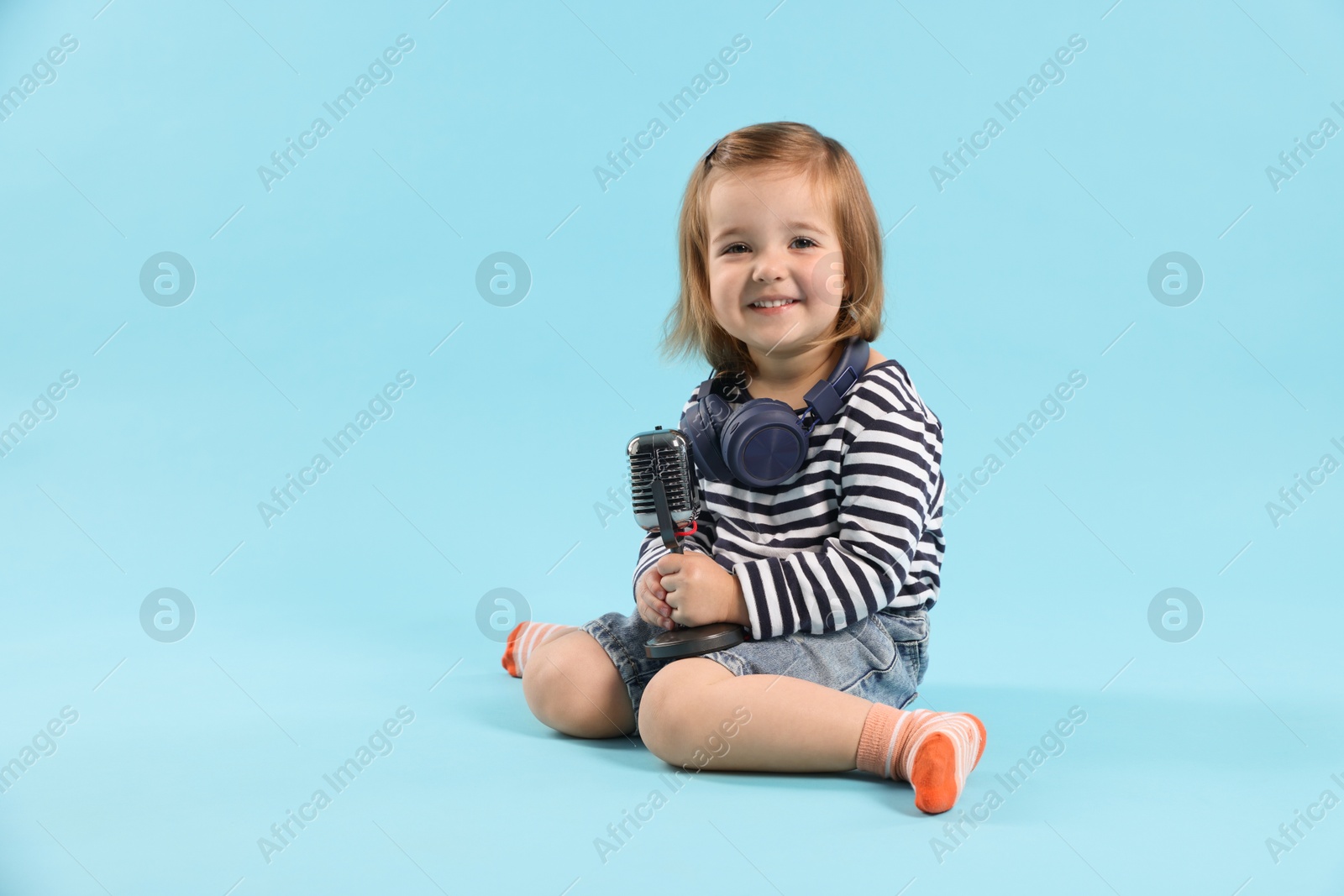 Cute little girl with headphones and microphone on light blue background Photo of Cute little girl with headphones and microphone on light blue background