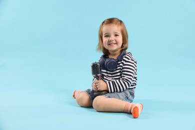 Photo of Cute little girl with headphones and microphone on light blue background