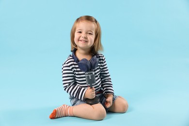Photo of Cute little girl with headphones and microphone on light blue background