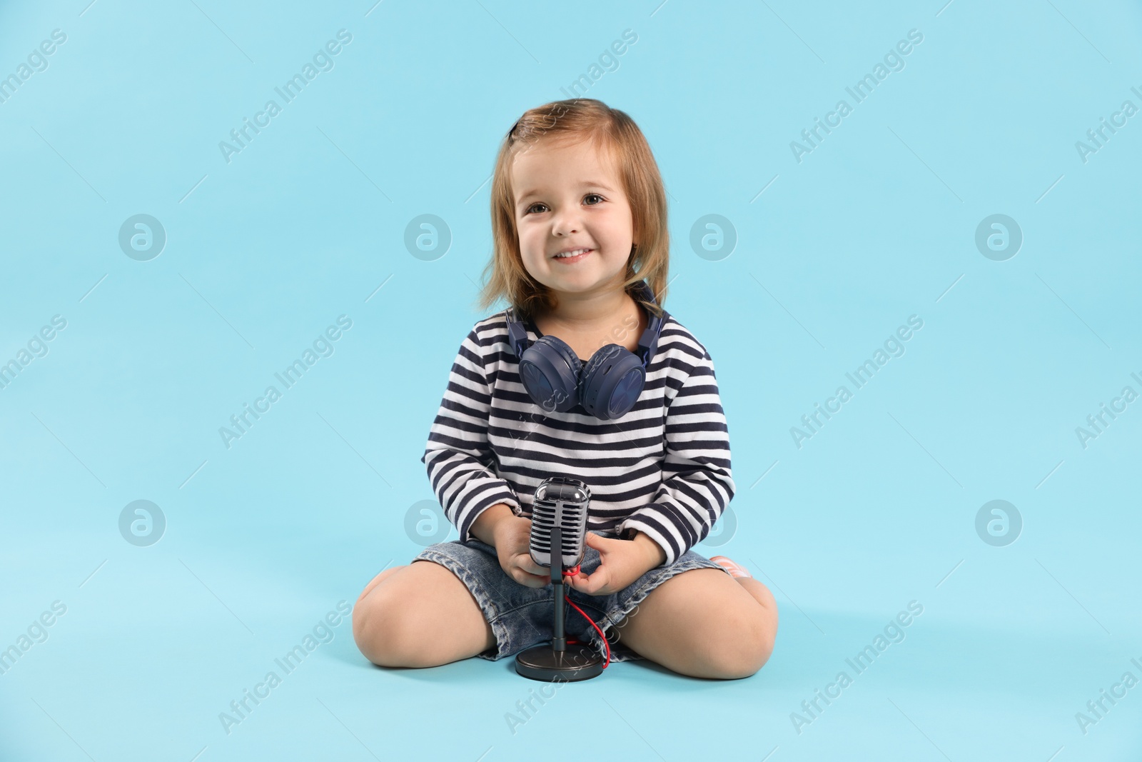 Cute little girl with headphones and microphone on light blue background Photo of Cute little girl with headphones and microphone on light blue background