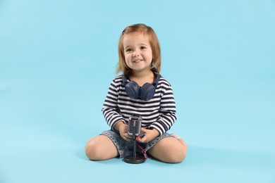 Photo of Cute little girl with headphones and microphone on light blue background
