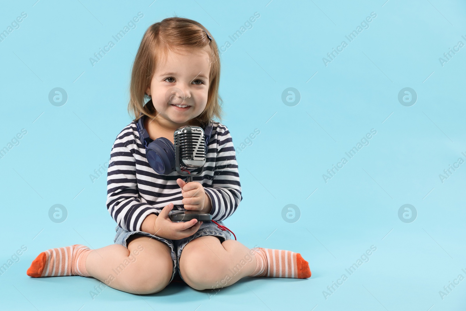 Cute little girl with headphones and microphone on light blue background, space for text Photo of Cute little girl with headphones and microphone on light blue background, space for text