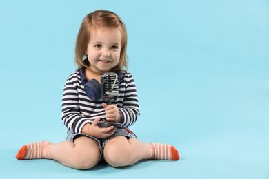Photo of Cute little girl with headphones and microphone on light blue background, space for text