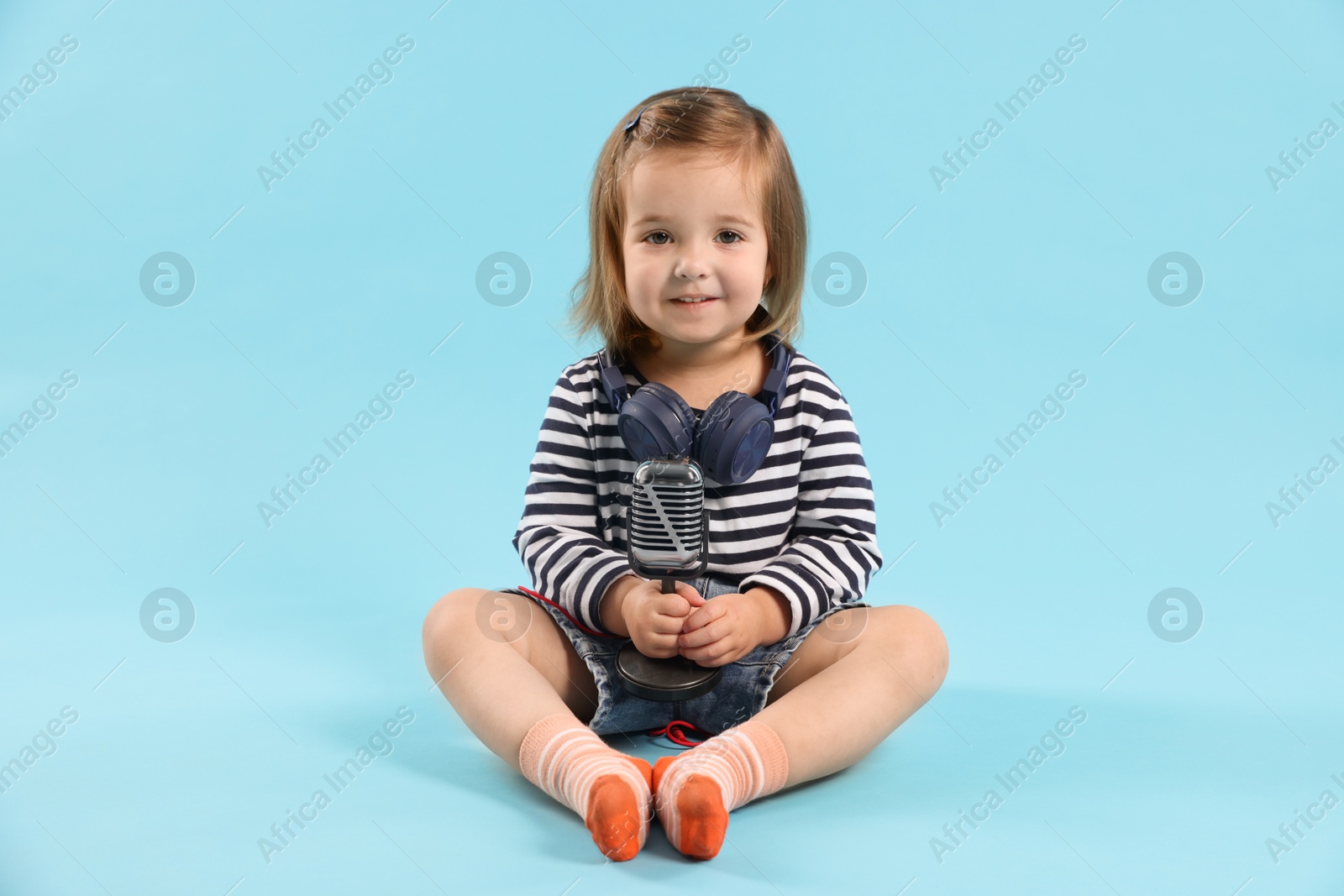 Cute little girl with headphones and microphone on light blue background Photo of Cute little girl with headphones and microphone on light blue background