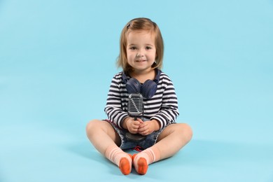 Photo of Cute little girl with headphones and microphone on light blue background