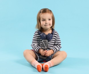 Photo of Cute little girl with headphones and microphone on light blue background