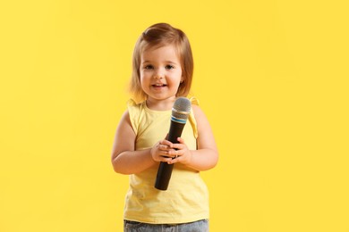 Photo of Cute little girl with microphone on yellow background