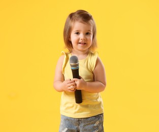 Photo of Cute little girl with microphone on yellow background