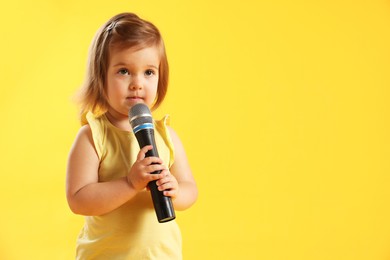 Photo of Cute little girl with microphone on yellow background, space for text